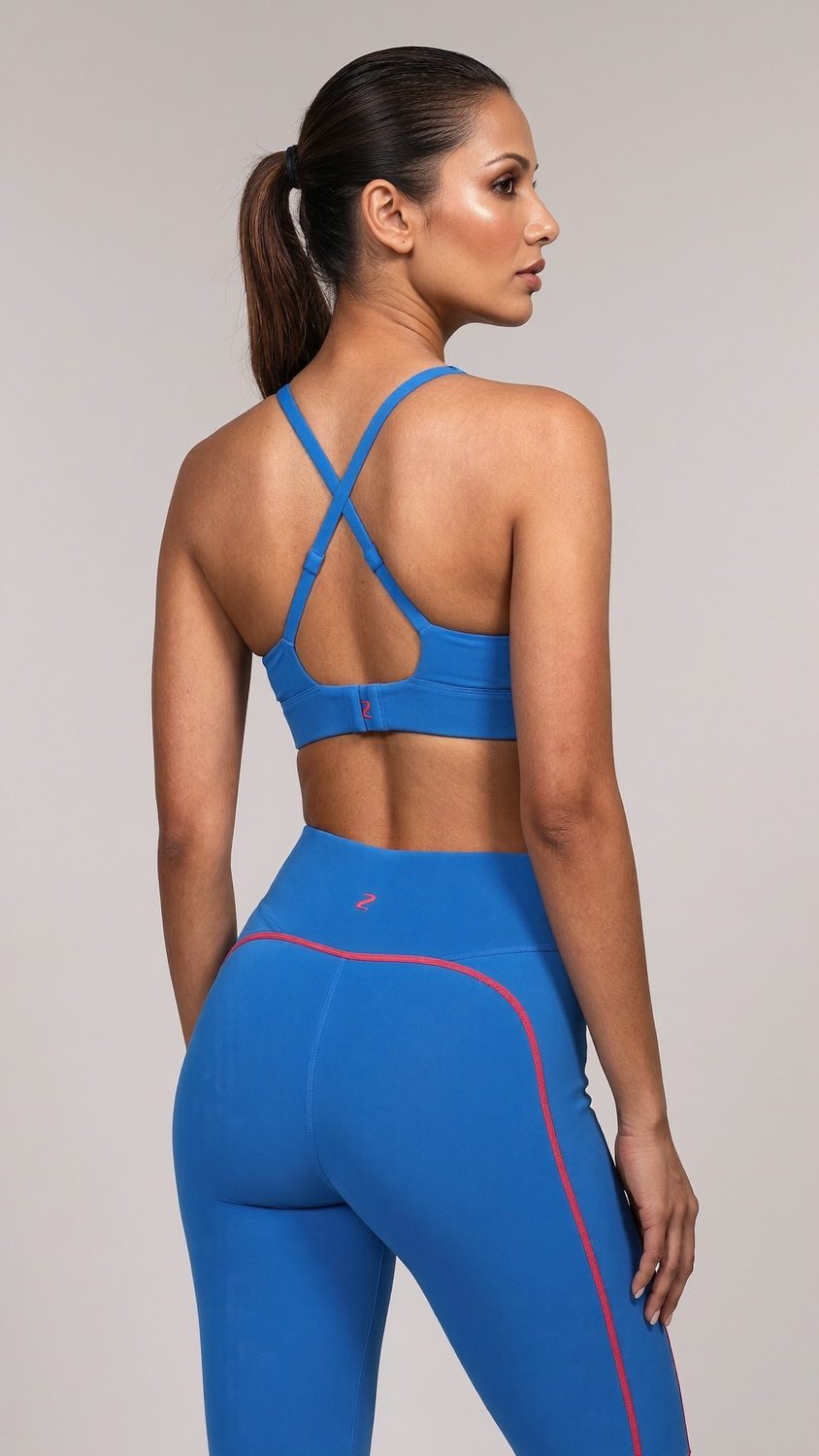 Back view of the blue cross-strap sports bra and leggings against a plain studio wall.